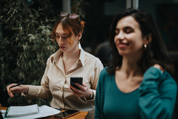 Two entrepreneurial women discuss startup strategies while sitting at a coffee bar, with gadgets and notes on the table.