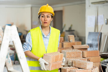 Young adult woman builder working at renovating object carrying bricks at construction site