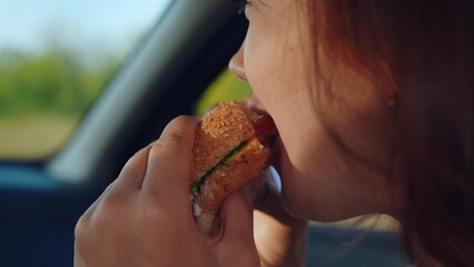 Young hungry woman eats roll with meatball while sitting in car. Girl passenger eats burger in car....