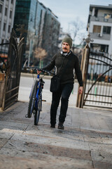 Man in winter attire walking with his bike on a city street, embodying urban lifestyle and eco-friendly transportation.