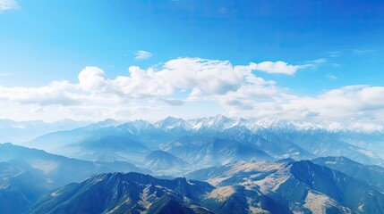 Fototapeta premium The mountain range is covered in snow. The sky is blue and cloudy. The sun is shining brightly. The mountains are in the distance.