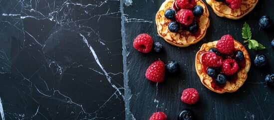 English-style crumpets topped with berries and honey, presented on a black marble surface, in a flatlay composition with space for text. - obrazy, fototapety, plakaty