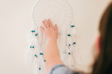 Dream Catcher.girl hangs a white dream catcher with white feathers and blue beads on a beige...