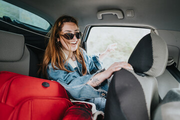 A cheerful young woman wearing sunglasses is laughing while sitting in the backseat of a car, signaling a sense of adventure and freedom.