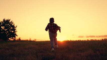Kid is running across field. Child boy runs through green grass in sun. Childhood dream happiness...