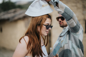 A young man adjusts a woman's hat as they examine a map together, enjoying their holiday in a quaint, historic village.