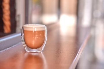 A transparent glass of latte stands outdoors on the tabletop of a coffee shop
