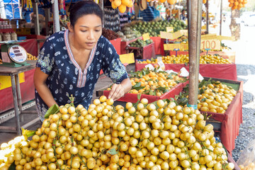 A young woman is standing near a tropical fruit the Burmese grape, in the market, Thailand