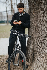 Young man resting and using smart phone next to bicycle in park setting.