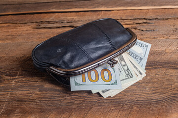 Top view of old black genuine leather wallet with banknotes inside wooden background.