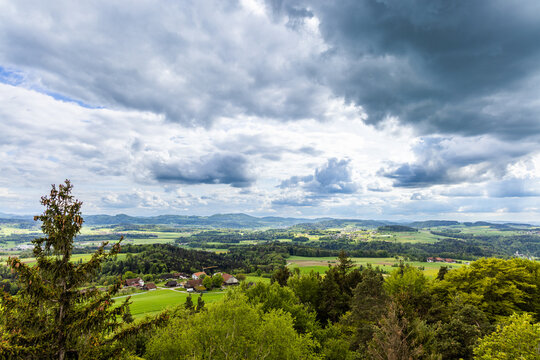 View of a forest, fields and village on the hills against a cloudy sky