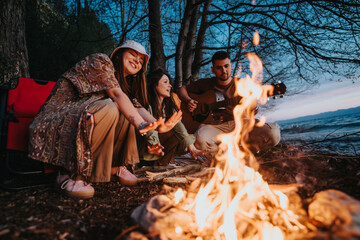 A group of friends gather around a warm campfire in the forest, enjoying live guitar music and a peaceful evening.