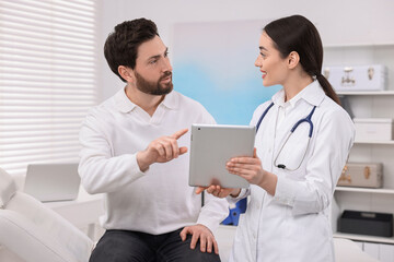 Doctor with tablet consulting patient during appointment in clinic