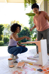Biracial mother and adult daughter painting furniture outdoors at home in an upcycling project - 788839909