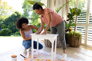 Biracial mother and adult daughter painting furniture outside at home in an upcycling project - 788839910