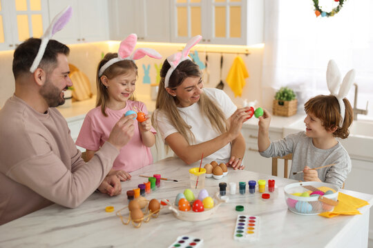 Easter celebration. Happy family with bunny ears having fun while painting eggs at white marble table in kitchen
