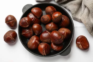 Schilderijen op glas Fresh edible sweet chestnuts in frying pan on white tiled table, flat lay © New Africa