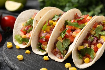 Tasty tacos with vegetables on black table, closeup