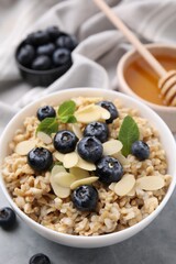Tasty oatmeal with blueberries, mint and almond petals in bowl on grey table, closeup