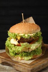 Burger with delicious patty on wooden table against dark background