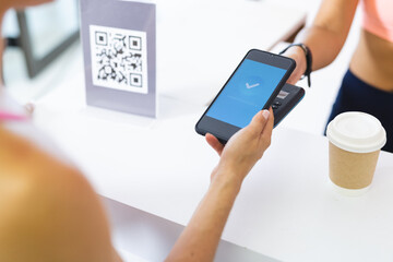 Biracial and Caucasian women are at reformer pilates studio, one holding smartphone scanning QR code