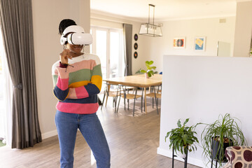 African American young woman at home in VR headset stands in living room at home, copy space