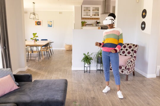 African American young woman in VR headset stands at home in living room at home, copy space