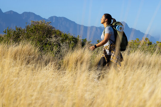 A biracial female hiker with a backpack is walking through tall grass, copy space