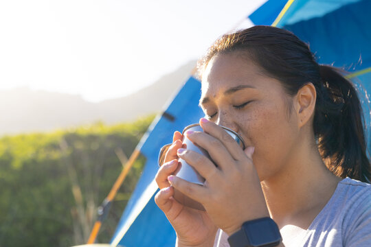 Biracial female hiker enjoying hot drink near tent, copy space