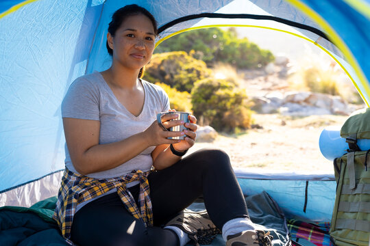 Biracial female hiker holding a cup, sitting in a tent