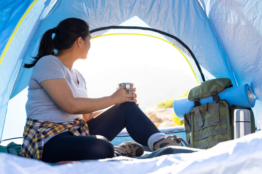 Biracial female hiker sitting inside tent, holding cup