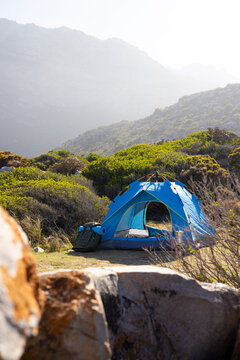 A blue tent stands alone in green, mountainous area, copy space