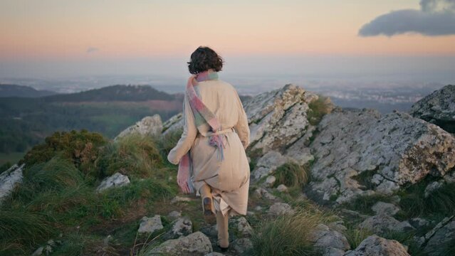 Tourist walking mountain path at twilight wearing coat. Elegant woman explorer