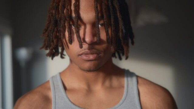 A young man with dreadlocks looking at the camera under the evening light. Slow motion. 