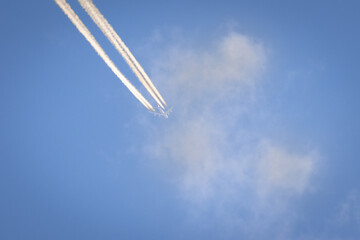 On the way in the sky.  Way above the clouds, a four engine jet airliner soars through the blue sky. Large transport aircraft makes contrails of vapor as it flies to its destination