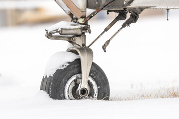 Airplane left in the snow. The nose gear wheel and tire sunk deep into a blanket of snowfall. Component of an airplane abandoned to the elements, to rot, decay, and corrode  - obrazy, fototapety, plakaty