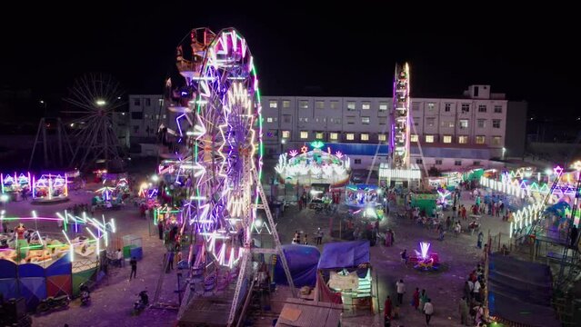 beautiful giant wheels with lights spinning at night drone orbit shot at exhibition in suraram, hyderabad, telangana, india. 4k night time