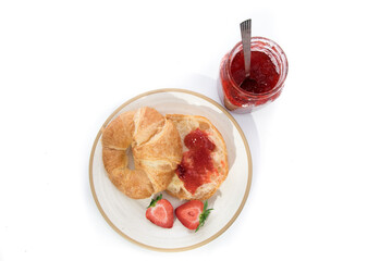 overhead view of a butter croissant on a plate with home made strawberry jam and a mason jar of jam isolated on white