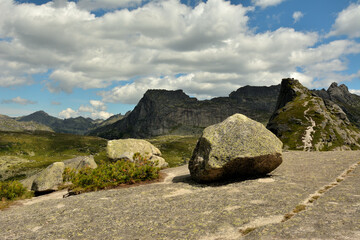 Large stones on top of a huge granite natural slab with a view of the picturesque mountains in the summer cloudy sky.