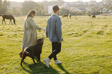 Stylish couple walking with a brown labrador on a nature