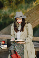 Young woman in a coat sitting on a wooden bench and reading a book