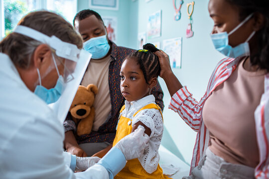 Child receiving vaccine with parents in doctor's office