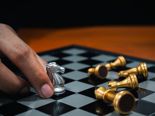 Golden horse, knight chess piece put by player's hand with silver pawn chess pieces, enemy on chessboard on dark background. Leadership, war victory, commander, competition, business strategy concept.