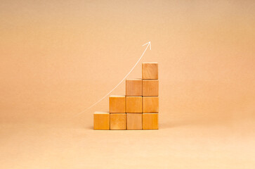 Rising up thin arrow on wooden cube blocks, bar graph chart steps on brown recycle paper background, profit, benefit, income, business growth process, economic improvement concepts, minimal style.