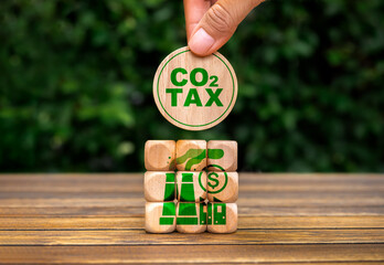 CO2, carbon TAX, global greenhouse gas emissions. Text "CO2 TAX" in hand put on cube puzzle stack wood blocks with green factory icon. Environmental and social responsibility business concept.