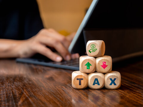 Save money icon, percent increase and decrease arrows, TAX, text on wooden cube blocks pyramid stack on table near businessman use laptop to tax calculated. Taxation, annual percentage rate concept.