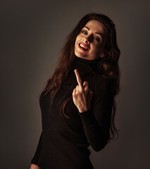 Fuck you. Beautiful smiling woman showing fuck off sign by middle finger in black clothing on dark studio background - 788893536