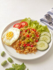 Fried rice with petai, fried egg, red chili and cellery, on white plate and white background. Indonesian typical food