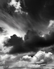 Clouds, very dramatic sky, in black and white. Grainy traditional analog style photo in ultra high resolution. Sunlight is pouting through the silhouette of the cloud formation. Moody, dark.