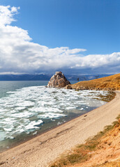 Spring on Baikal Lake. View of natural landmark - Shamanka Rock during ice drift on sunny May day. Sandy deserted beach on coast of Olkhon Island awaits tourists. Scenic landscape. Spring travels
